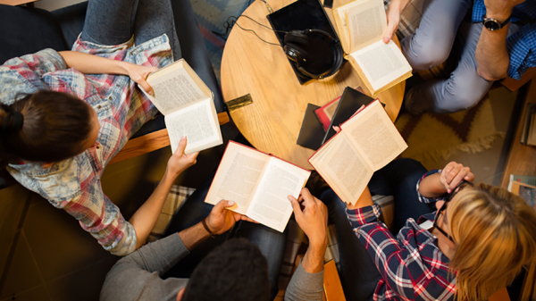 a photo looking down on a group of adults reading books around a small table